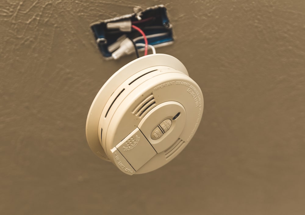 Interiror smoke alarm dangling by wires from the ceiling.